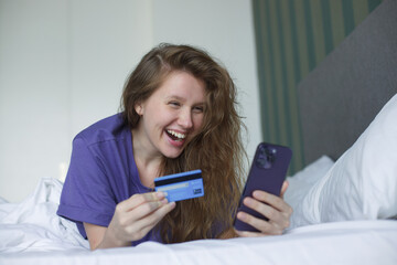 Portrait of happy excited amazed girl, shocked young successful joyful woman paying, holding credit bank card with phone, laptop celebrating victory, triumph, success at home. Online shopping