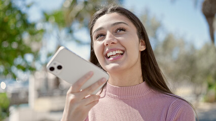 Young beautiful hispanic woman sending voice message with smartphone at park
