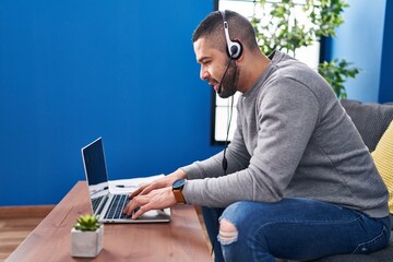 Young latin man using laptop and headphones sitting on table at home