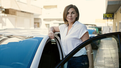 Middle age hispanic woman leaning on the car at street