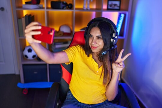 Young beautiful arab woman streamer smiling confident make selfie by smartphone at gaming room