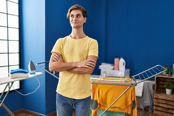 Young man doing laundry smiling looking to the side and staring away thinking.