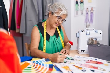 Middle age grey-haired woman tailor smiling confident drawing clothing design at tailor shop