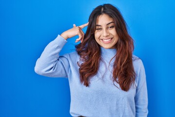 Fototapeta premium Hispanic young woman standing over blue background smiling pointing to head with one finger, great idea or thought, good memory