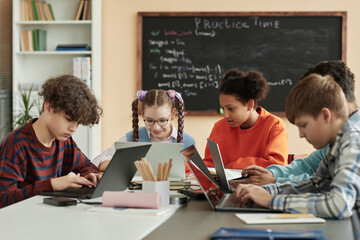 Diverse group of teen children using laptops in school classroom and studying together