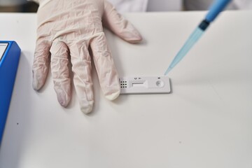 Young beautiful hispanic woman scientist pouring liquid to antigen test at pharmacy