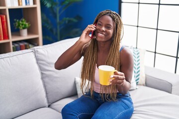 African american woman talking on smartphone drinking coffee at home