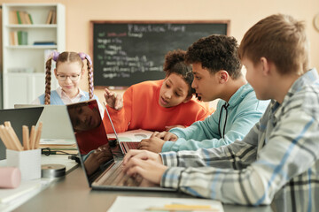 Fototapeta na wymiar Diverse group of children using laptops in school classroom with black girl peeking at computer screen
