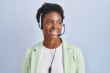 African american woman wearing call center agent headset looking away to side with smile on face,...