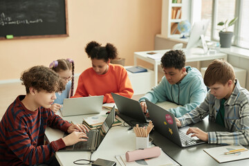 High angle view at diverse group of teen schoolchildren using computers in classroom studying...