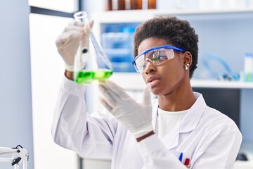 African american woman wearing scientist uniform measuring liquid at laboratory