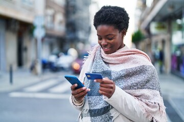 African american woman using smartphone and credit card at street