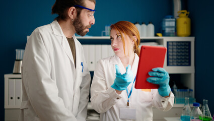 Man and woman wearing sciencist uniform using touchpad at laboratory