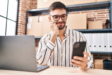 Young hispanic man ecommerce business worker using laptop and smartphone at office