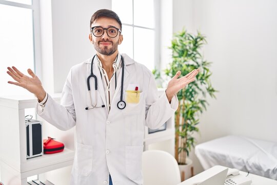 Hispanic man wearing doctor uniform and stethoscope shouting and screaming loud to side with hand on mouth. communication concept.