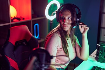 Young beautiful hispanic woman streamer sitting on table with serious expression at gaming room