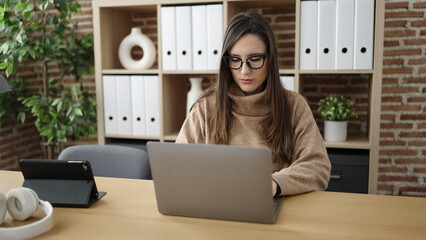 Beautiful hispanic woman business worker using laptop with serious face at office