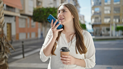 Fototapeta premium Young beautiful hispanic woman sending voice message by smartphone drinking coffee at street