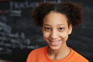 Closeup portrait of black teenage girl by blackboard in school classroom smiling at camera, copy...