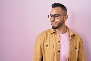 Obraz premium Young hispanic man standing over pink background looking away to side with smile on face, natural expression. laughing confident.