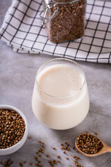 Lactose free dietary buckwheat milk in a glass and seeds in a bowl on the table vertical view