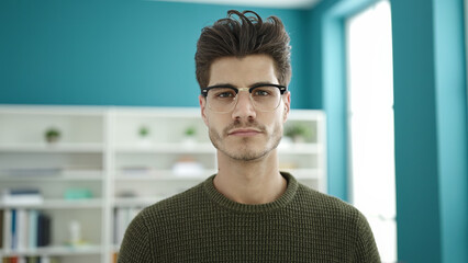 Young hispanic man student standing with relaxed expression at library university