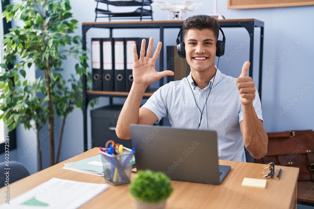 Sticker young hispanic man working at the office wearing headphones showing and pointing up with fingers num