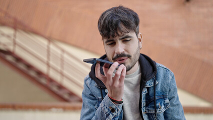 Young hispanic man sending voice message with smartphone at street