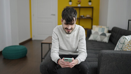 Young hispanic man using smartphone sitting on the sofa at home