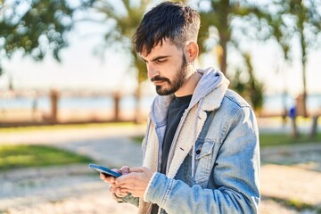 Fototapeta premium Young hispanic man using smartphone at park