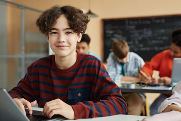 Portrait of teen boy with curly hair looking at camera at desk during school class, copy space