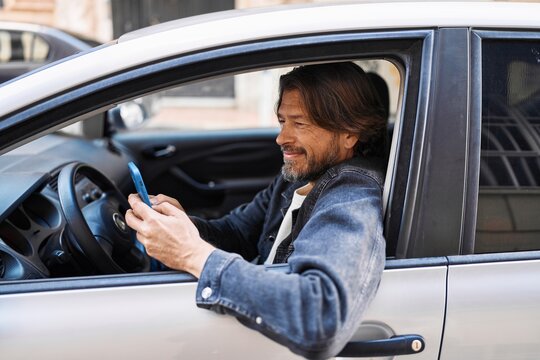 Middle age man using smartphone sitting on car at street