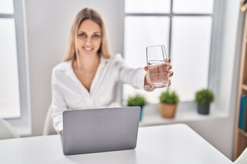 Young woman using laptop drinking water sitting on table at home