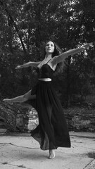 Full length of a ballerina in a black dress doing a pirouette outside. Black and white image.