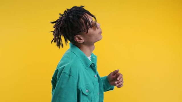 Energetic african man dancing on yellow background. Stylish guy with dreadlocks