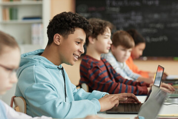 Side view at teen schoolboy using computer in row in school classroom and taking online exam