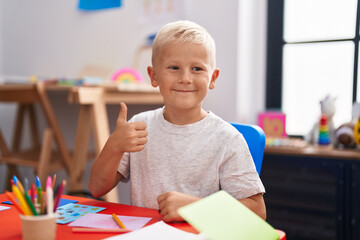 Little caucasian boy painting at the school smiling happy and positive, thumb up doing excellent and approval sign