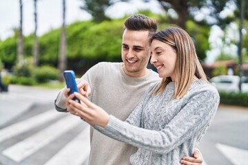 Man and woman couple hugging each other using smartphone at street