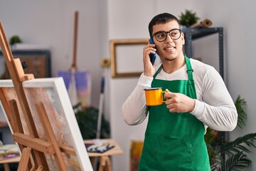 Young man artist talking on the smartphone drinking coffee at art studio