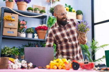 Young bald man florist using laptop holding plant at flower shop