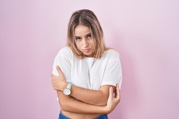 Obraz premium Young blonde woman standing over pink background shaking and freezing for winter cold with sad and shock expression on face