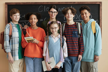 Front view portrait of diverse group of children looking at camera standing by blackboard in class