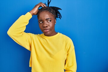 Beautiful black woman standing over blue background confuse and wondering about question. uncertain...