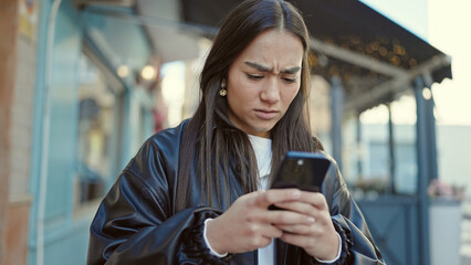 Young beautiful hispanic woman using smartphone with serious expression at coffee shop terrace