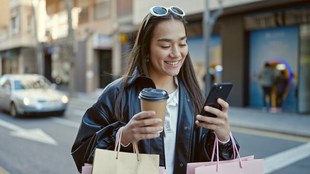 Young beautiful hispanic woman using smartphone holding shopping bags and coffee at street