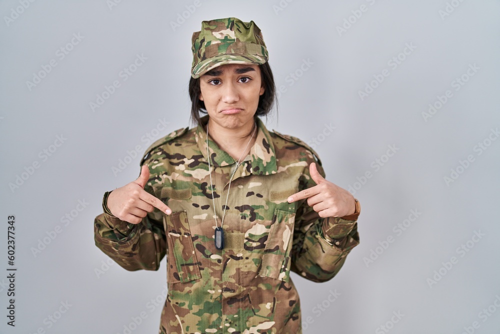 Poster young south asian woman wearing camouflage army uniform pointing down looking sad and upset, indicat