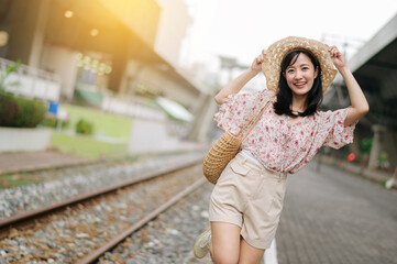 young asian woman traveler with weaving basket happy smiling looking to a camera beside train railway. Journey trip lifestyle, world travel explorer or Asia summer tourism concept.