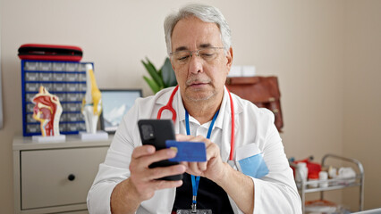 Middle age man with grey hair doctor using smartphone working doing online shopping at clinic