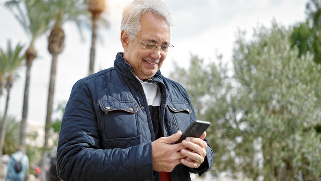 Middle age man with grey hair using smartphone smiling at park