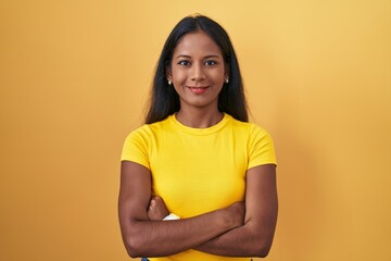 Obraz premium Young indian woman standing over yellow background happy face smiling with crossed arms looking at the camera. positive person.